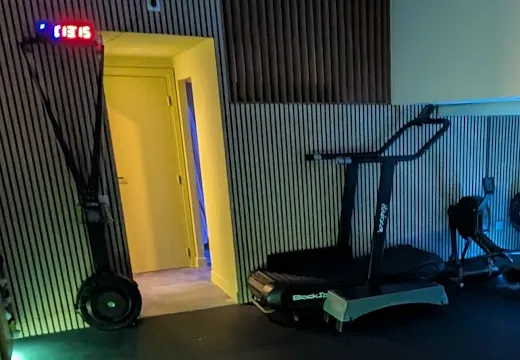 Le chrono rouge au-dessus de la porte, le ski erg et le tapis incurvé du studio, éclairés aux LED