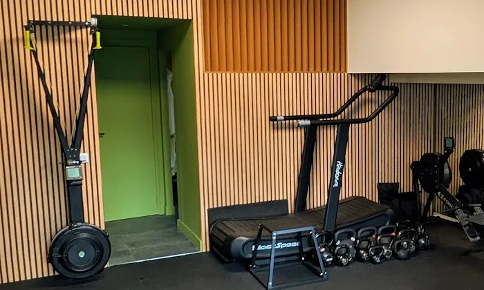 Ski erg, tapis de course incurvé et rangée de kettlebells devant le mur en bois du studio